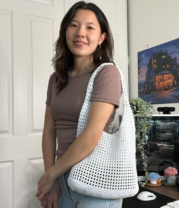 a woman standing in front of a computer desk holding a white bag over her shoulder