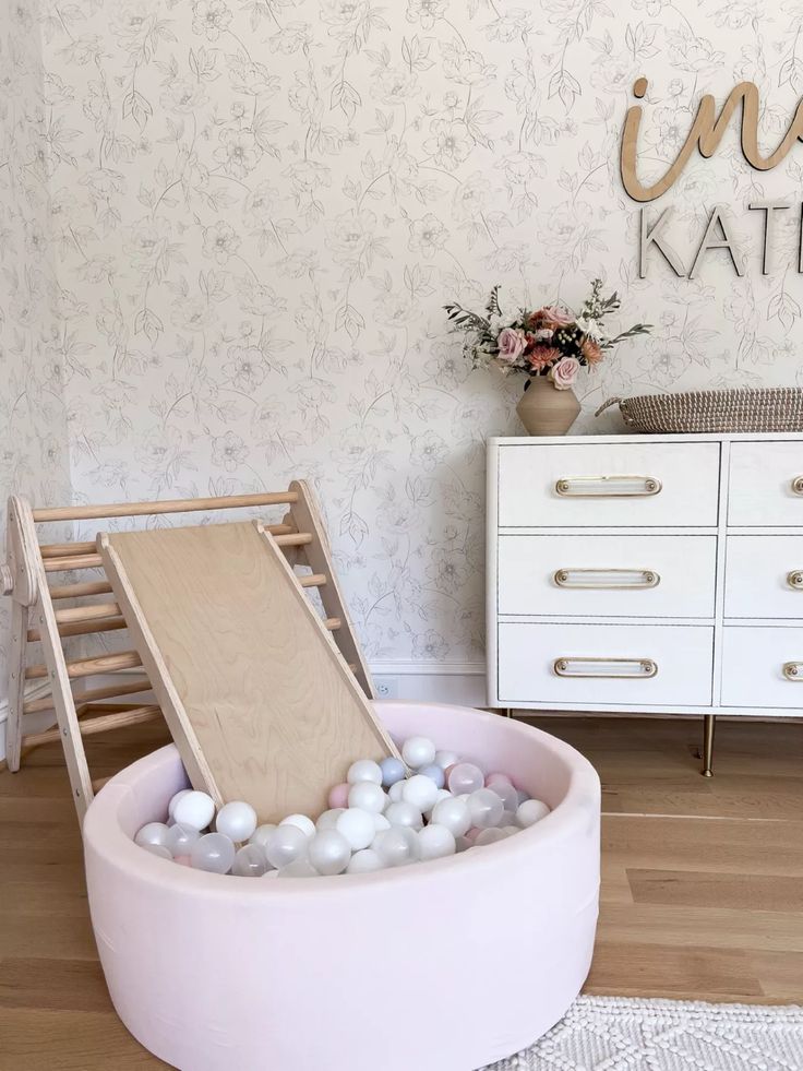 a pink chair with white balls in it and a wooden slide on the back wall