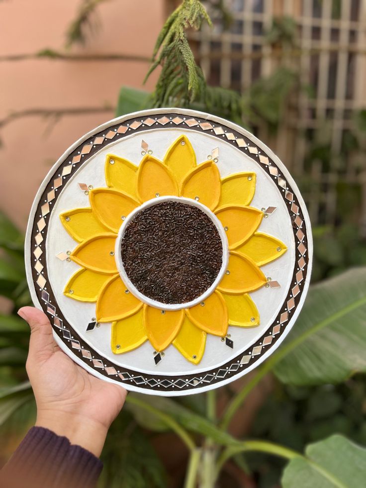 a hand holding a decorative plate with a sunflower on it