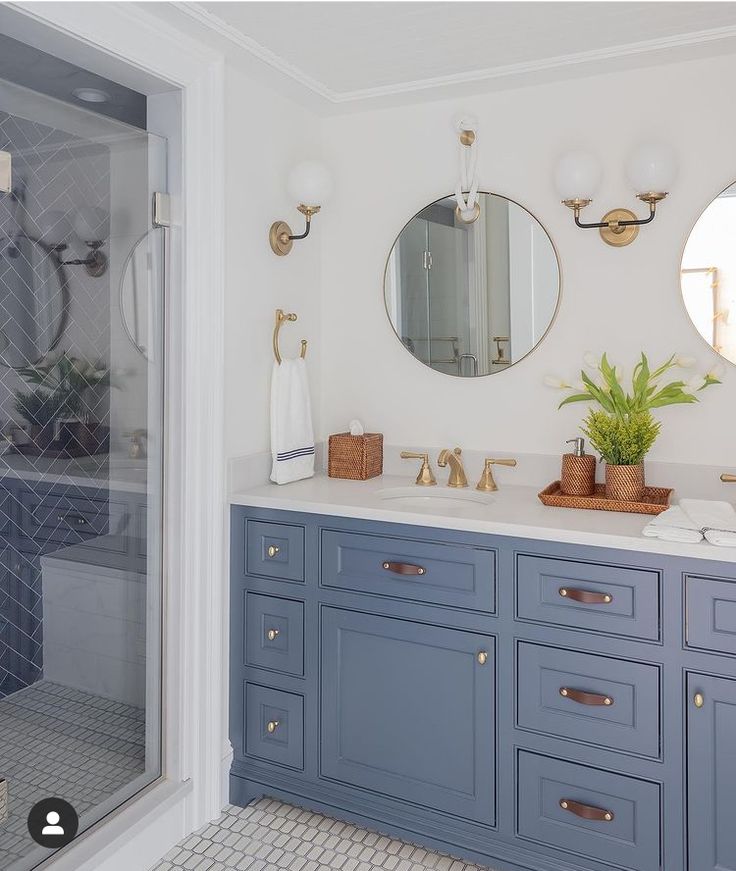 a bathroom with blue cabinets and gold fixtures on the countertop, along with a round mirror