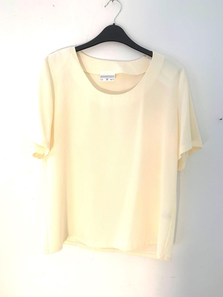 Pale yellow Vintage Blouse Semi Sheer Button Through Boxy Shirt Sleeves - Size 14 Introducing our stunning Pale Yellow Vintage Blouse, the perfect addition to any wardrobe for those who appreciate timeless, classic style. This semi-sheer blouse boasts a button-through front, allowing for versatility in styling options, while its boxy silhouette offers a relaxed and comfortable fit. Crafted from high-quality, lightweight fabric, this blouse is perfect for any occasion. The pale yellow hue adds a Elegant Beige Crew Neck Blouse, Cream Short Sleeve Workwear Shirt, Elegant Yellow Summer Shirt, Classic Cream Tops For Summer, Cream Short Sleeve Blouse For Summer, Beige Crew Neck Blouse For Work, Vintage Crew Neck Blouse For Summer, Vintage Short Sleeve Beige Blouse, Vintage Beige Short Sleeve Blouse