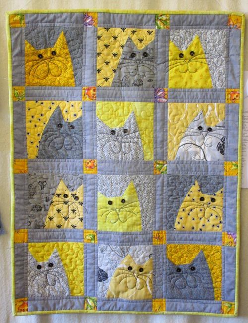 a quilted wall hanging with cats on it's sides and yellow, gray, and white squares