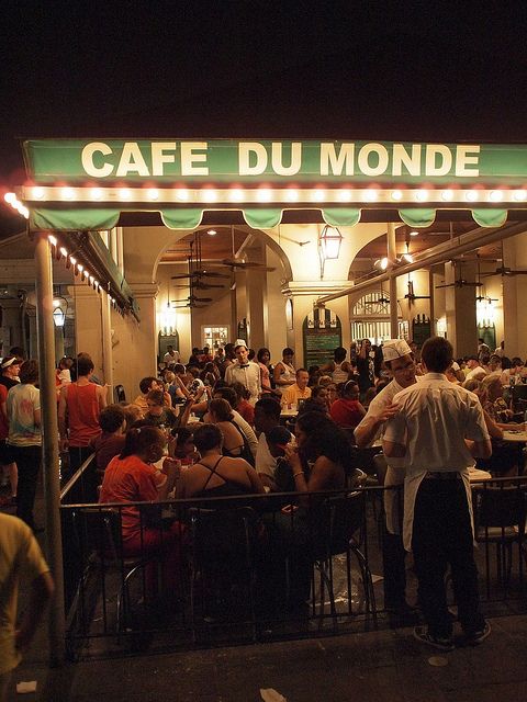 a group of people sitting at tables in front of a restaurant with lights on it