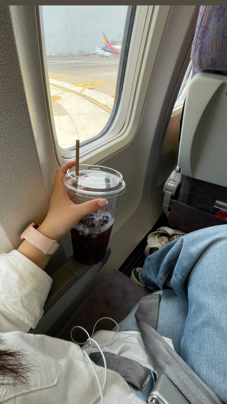 a person holding a drink in front of an airplane window