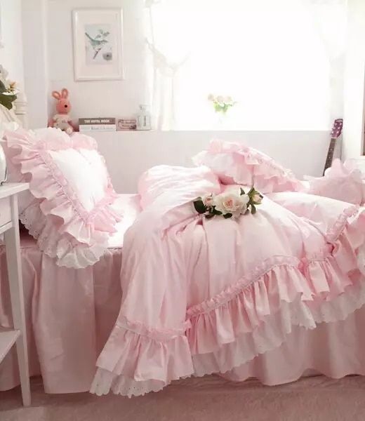 a bed with pink ruffles and pillows in a room next to a window