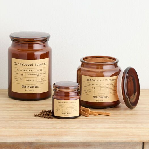 three jars of candles sitting on top of a wooden table next to a cup and matches