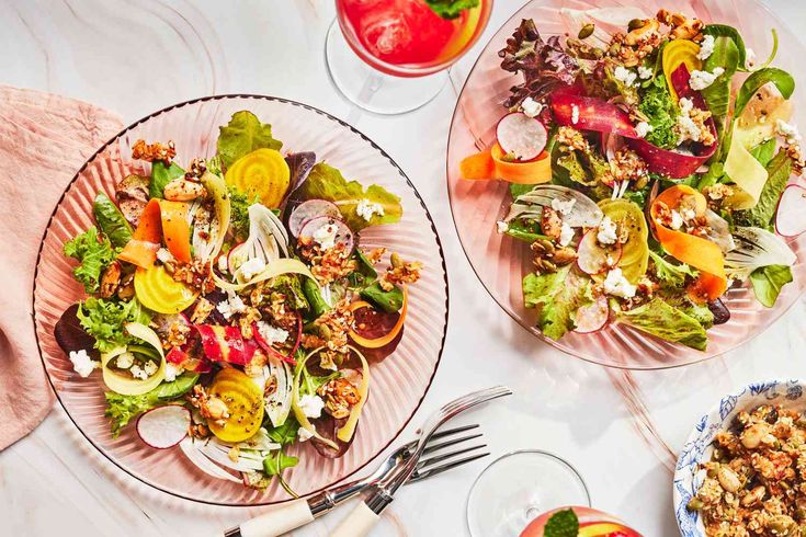 two plates filled with salad on top of a table next to glasses and utensils