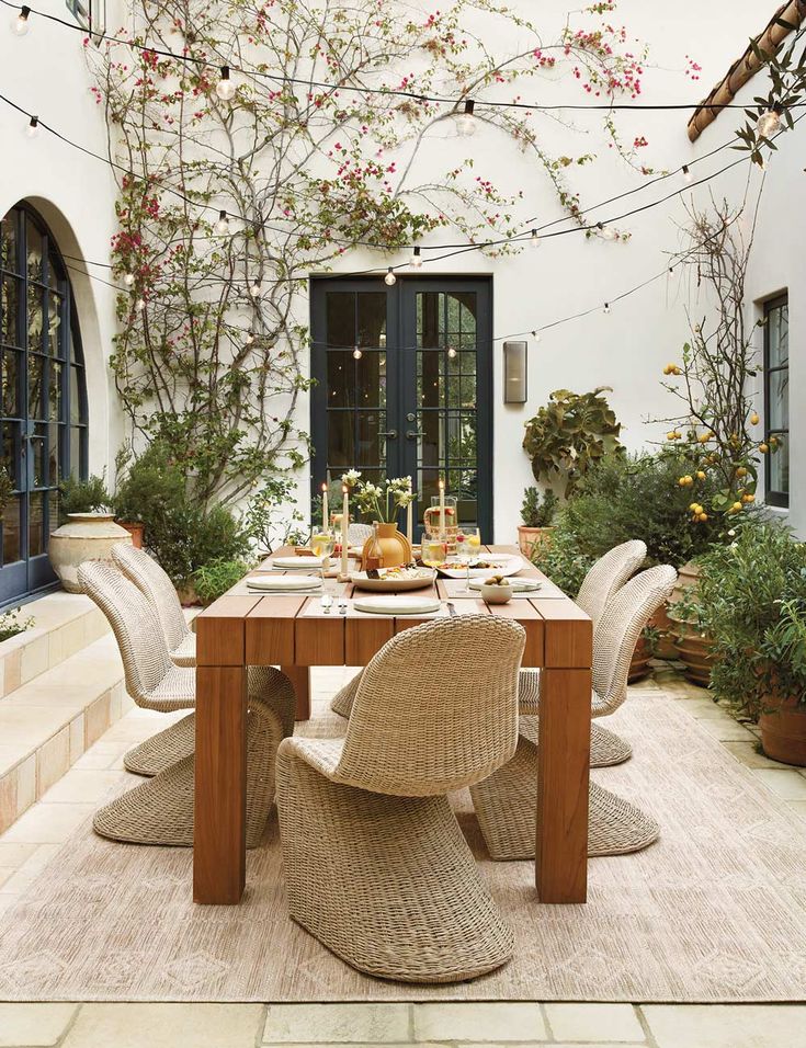 an outdoor dining area with wicker chairs and wooden table surrounded by potted plants