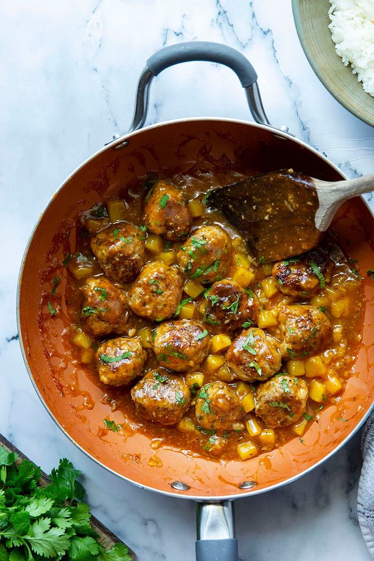 a pan filled with meatballs and corn on top of a table next to rice