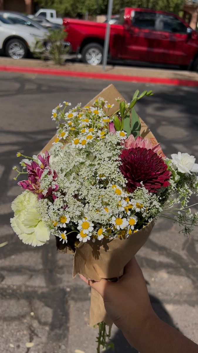 a person holding a bouquet of flowers in front of a red car on the street