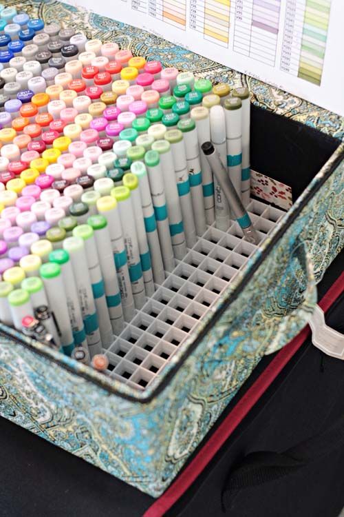 a desk with many pens and markers in it on top of a black box next to a computer keyboard