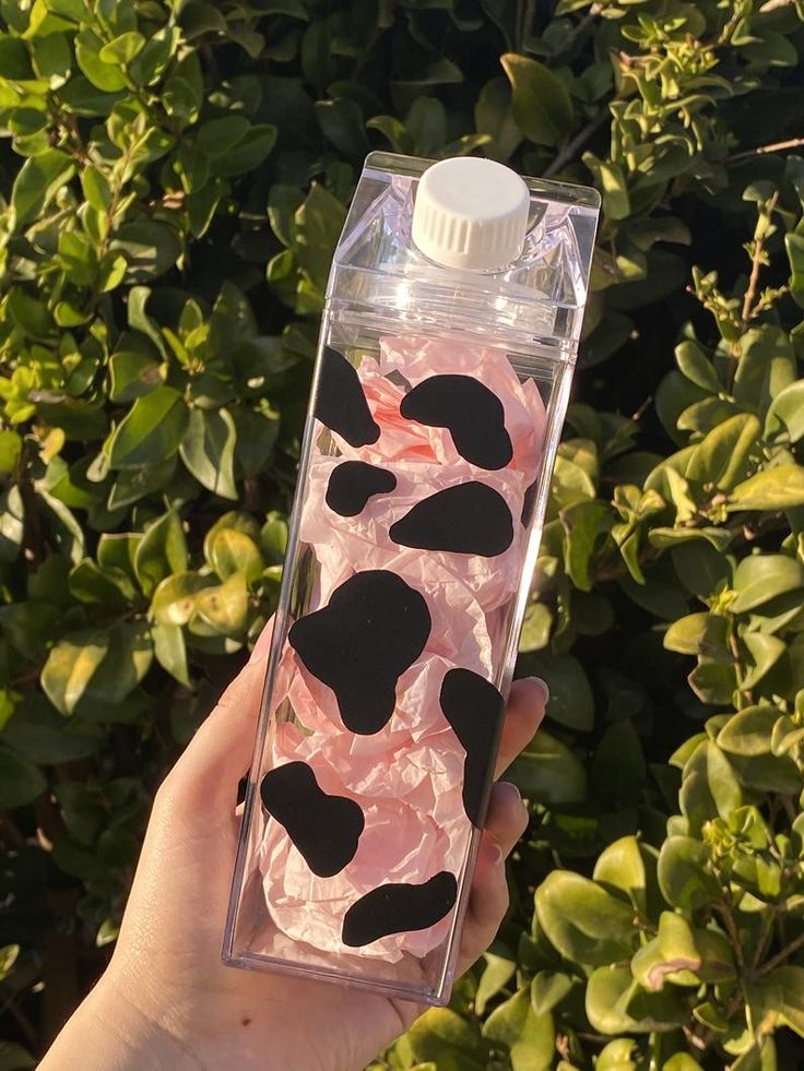 a hand holding a water bottle filled with pink and black liquid in front of bushes