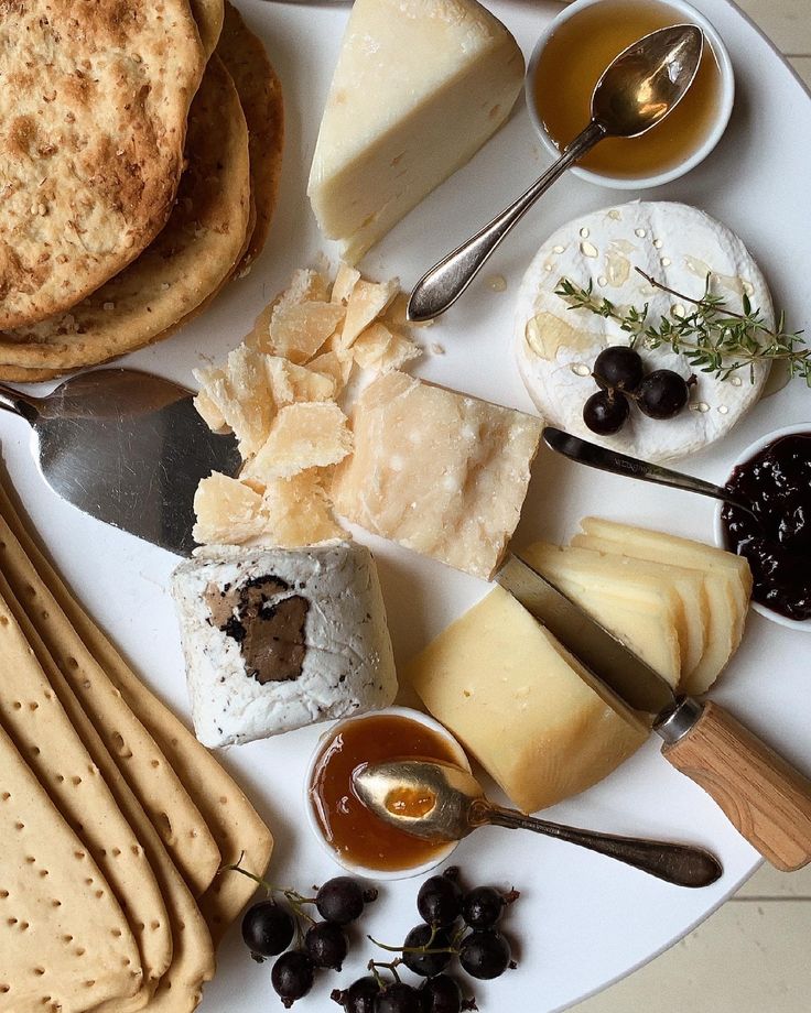 a white plate topped with lots of different types of cheese and crackers next to olives