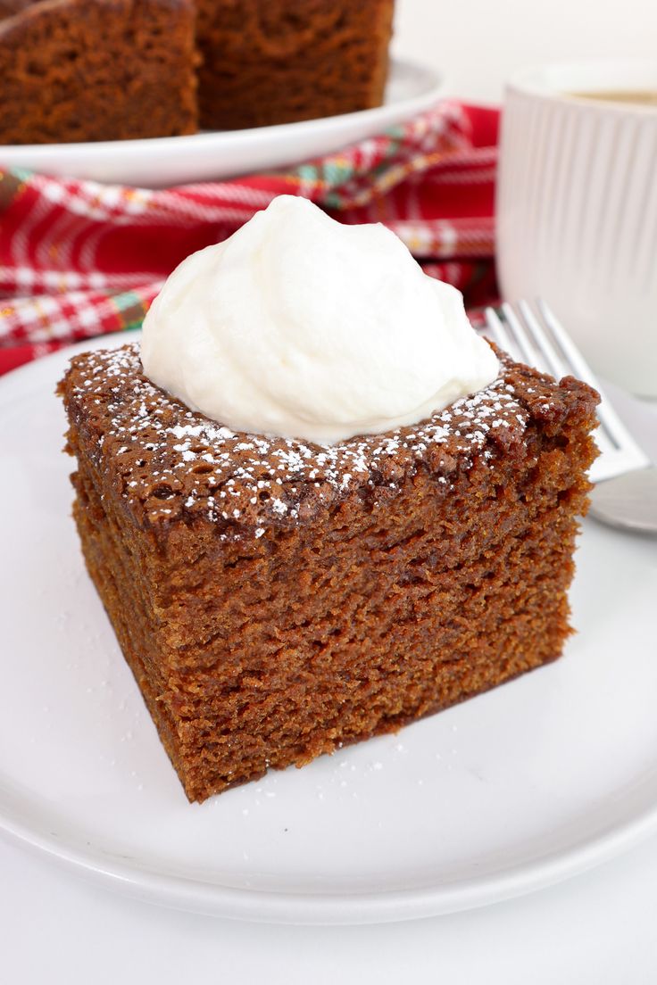 a piece of cake on a white plate with a cup of coffee in the background