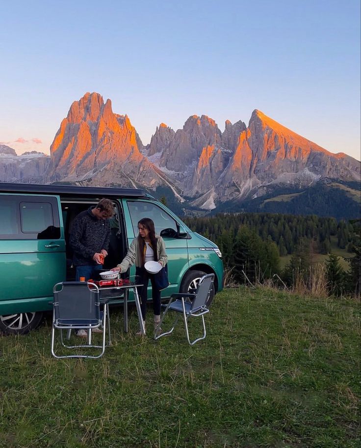 two people sitting at a table in front of a van with mountains in the background