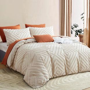 a bed with orange and white comforters in a bedroom next to a plant on the window sill