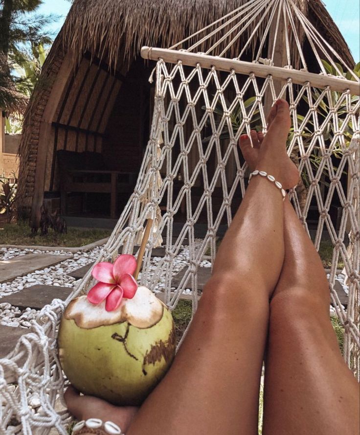 a person laying in a hammock with a coconut drink