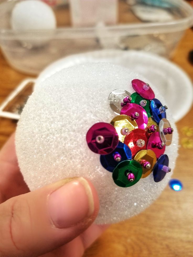 a hand holding a small white object with colorful buttons on it's center piece