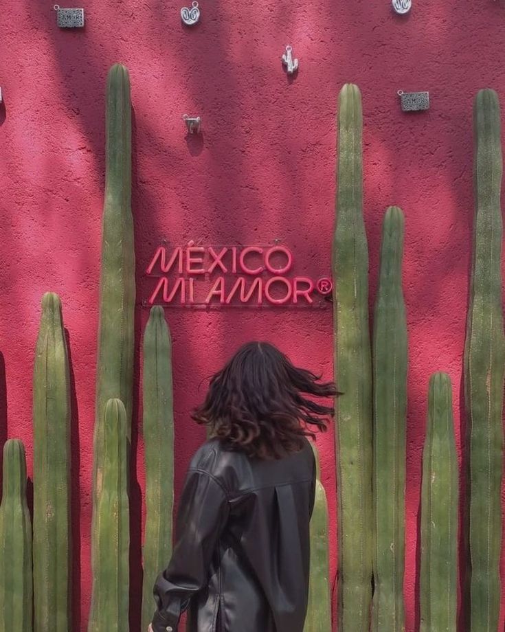 a woman standing in front of a pink wall with cactus plants and a sign that reads mexico miamor