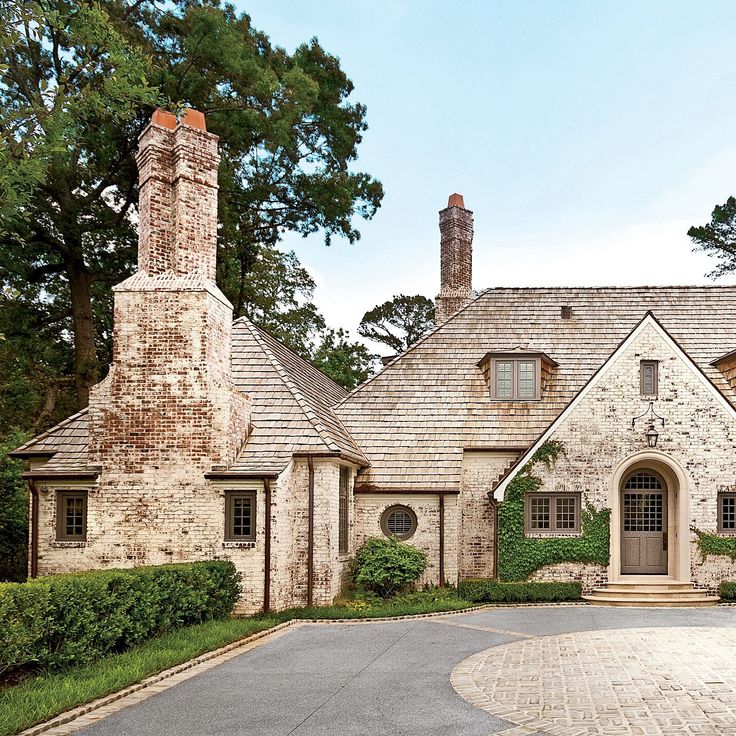 a large brick house with two chimneys on the front and one in the back that is surrounded by greenery