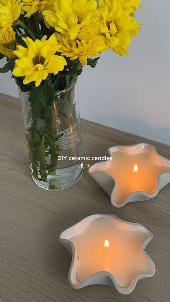 yellow flowers in a glass vase and two white dishes with candles on a wooden table