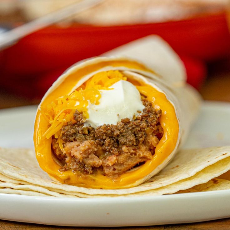 a burrito on a plate with sour cream and ground beef in the center, topped with cheese