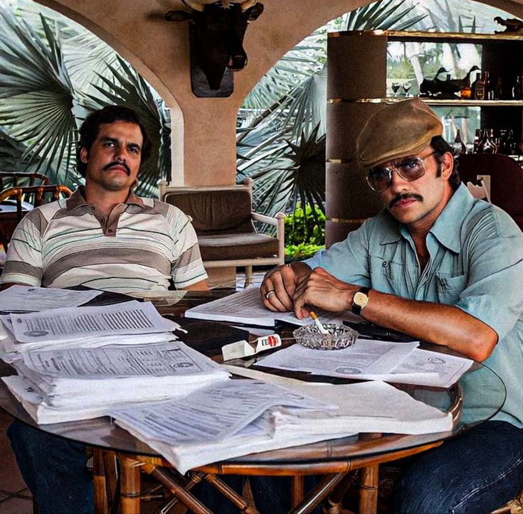 two men sitting at a table with papers and pens in front of them on top of each other