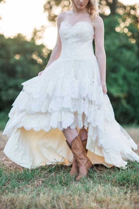 a woman wearing cowboy boots and a white dress is standing in the grass with her hands on her hips