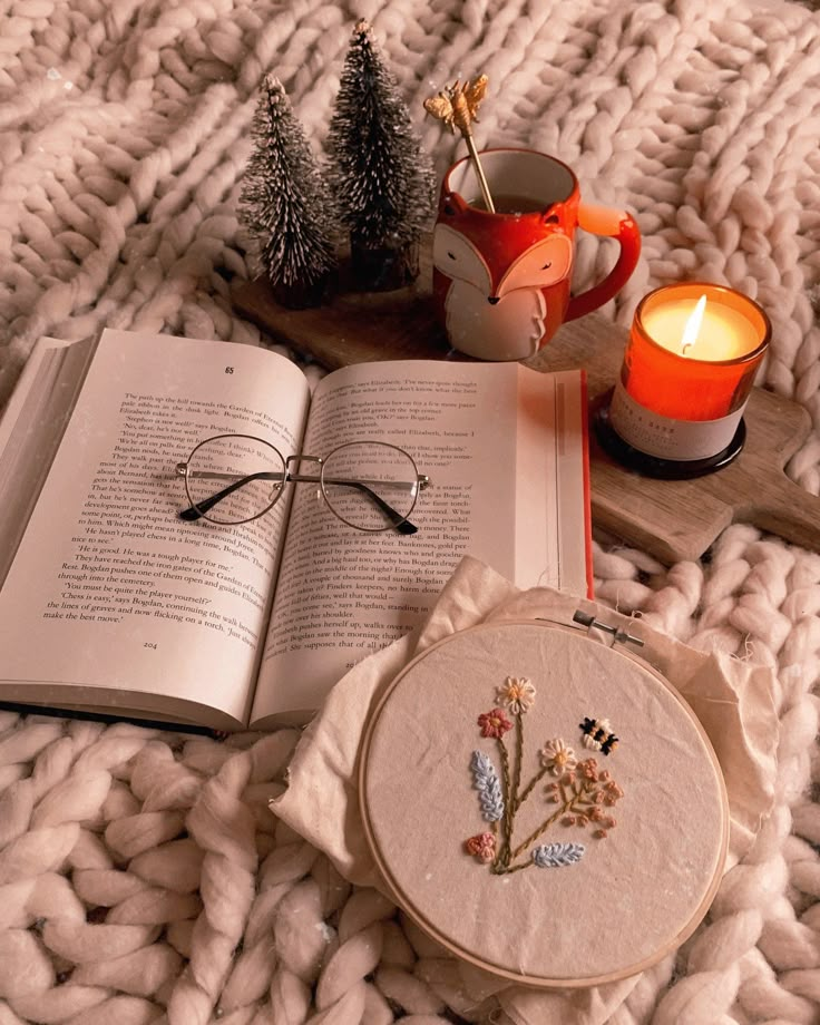 an open book and glasses on top of a white blanket next to a tea cup