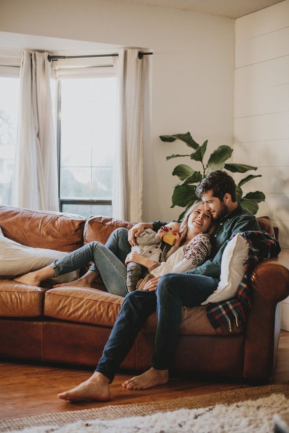 a man and woman sitting on a couch with a baby in their lap, smiling at the camera