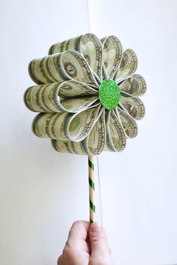 a hand holding a green and white pinwheel made out of money