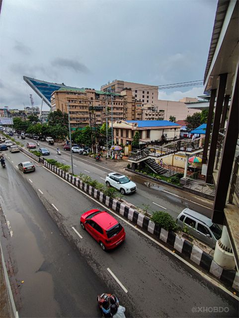 a red car driving down a street next to tall buildings on either side of the road