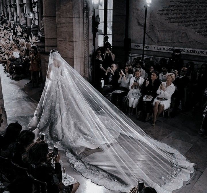 a woman in a white wedding dress and veil walking down the runway at a fashion show