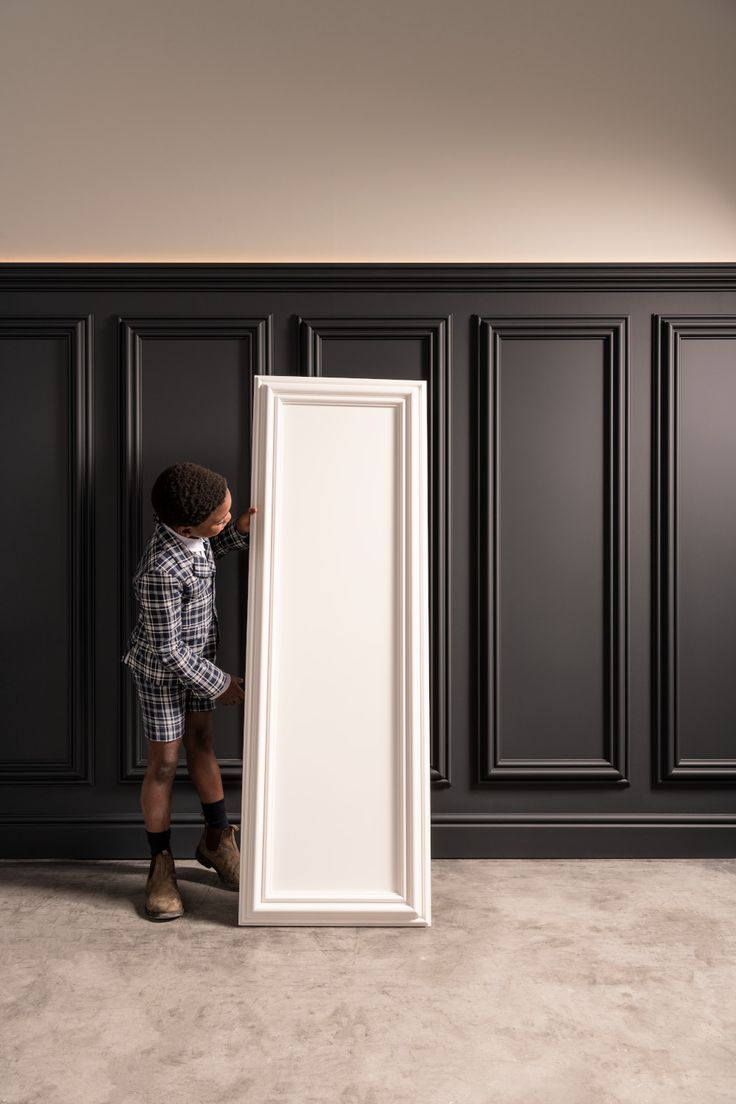 a young man standing in front of an empty white door with his hands on the frame