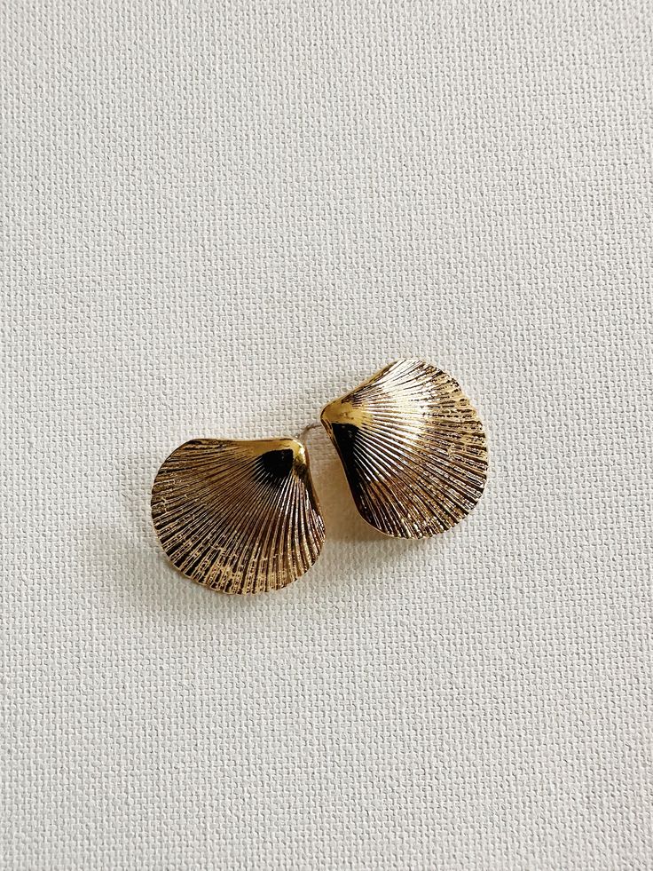 two seashells are sitting on a white surface, one is gold and the other is silver