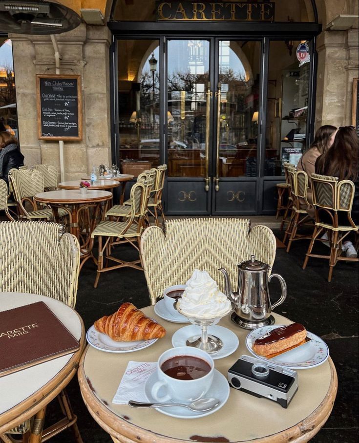 a table with coffee, croissants and pastries on it in front of a cafe