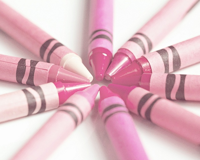 pink crayons arranged in a star shape on a white table top, with black and gray stripes