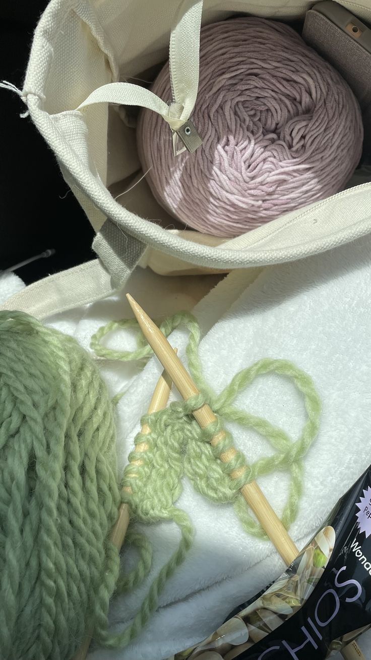 two skeins of yarn sitting in a bag next to knitting needles and a crochet hook