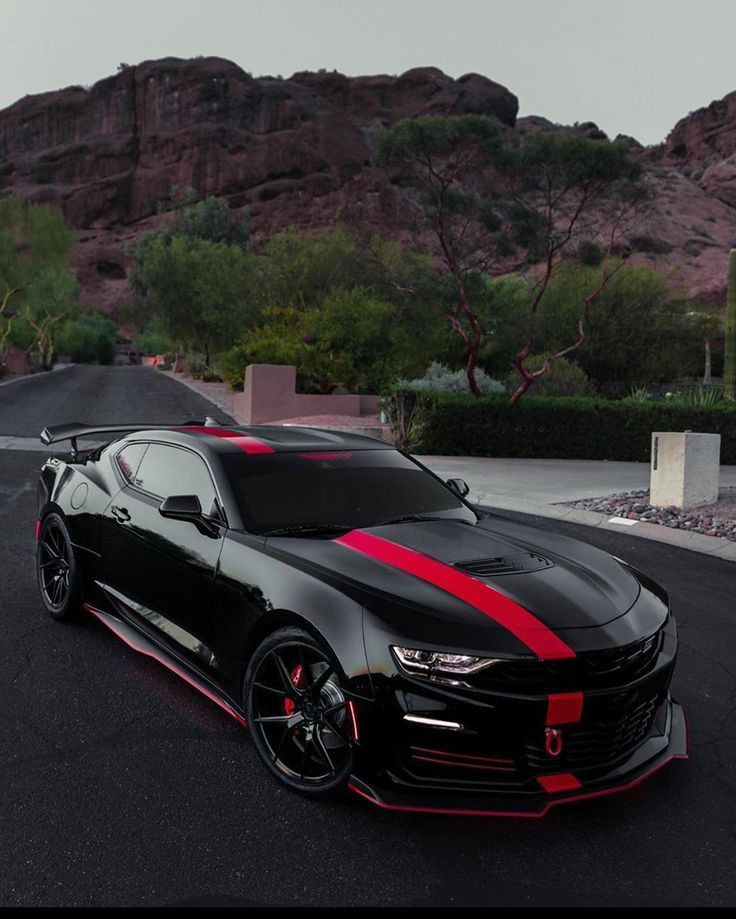 a black car with red stripes parked on the side of a road in front of mountains