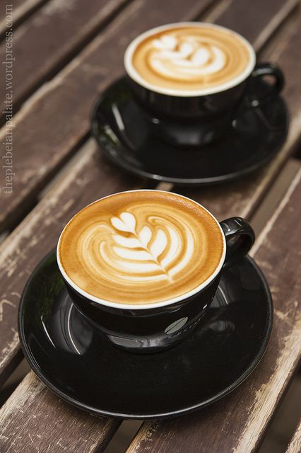 two cups of coffee sitting on top of a black saucer next to each other