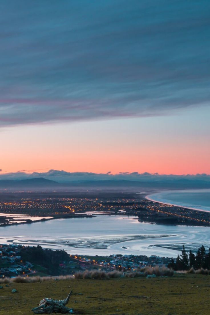 the sky is pink and blue as the sun sets over a lake with mountains in the background