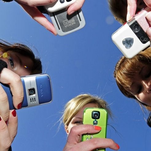 four people holding up their cell phones in the air with one woman's hand