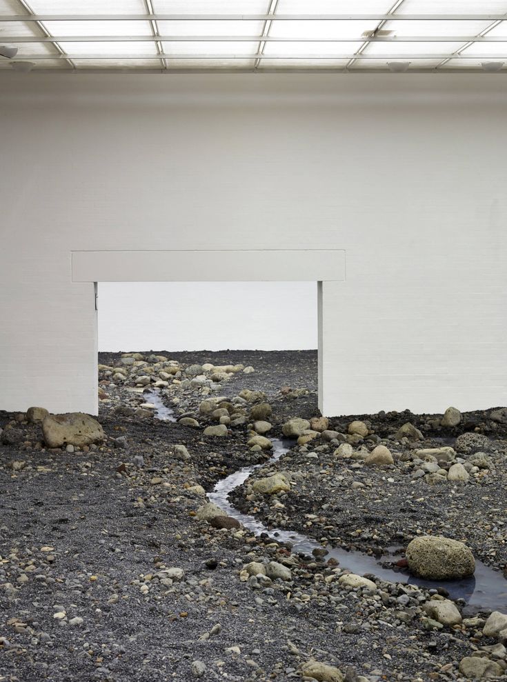 an empty room with rocks and water running through the floor, in front of a white wall