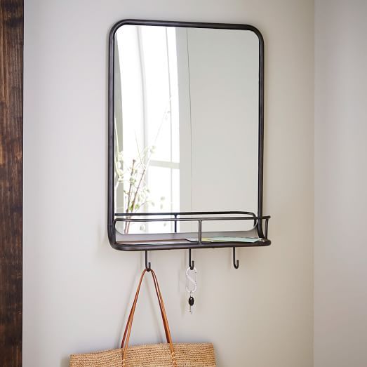 a mirror hanging on the wall next to a wooden shelf with a handbag in front of it