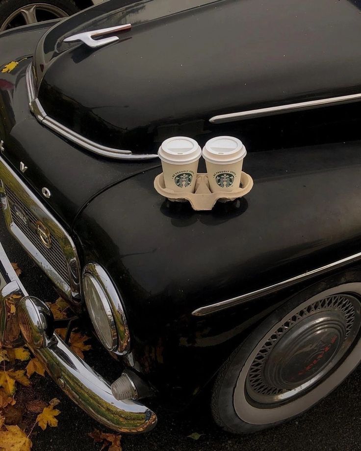 two coffee cups are placed on the hood of an old car