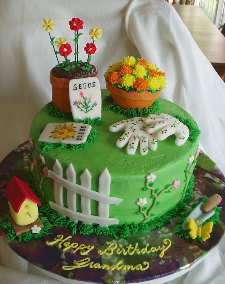 a green birthday cake with flowers and plants on top, sitting on a table in front of a white chair