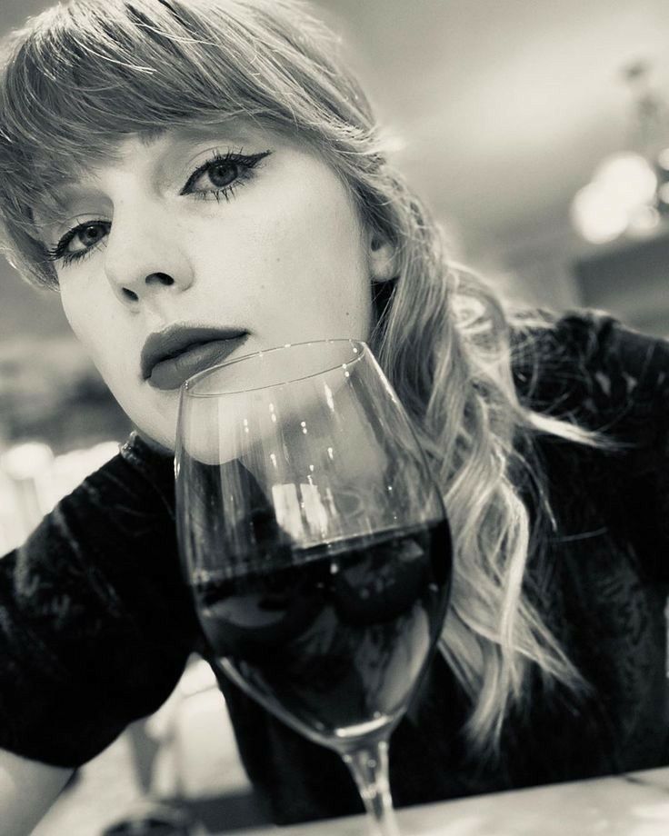 a woman sitting at a table with a glass of wine in front of her face