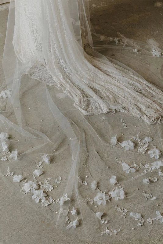 a wedding dress with white flowers on the bottom, and veil over it's head