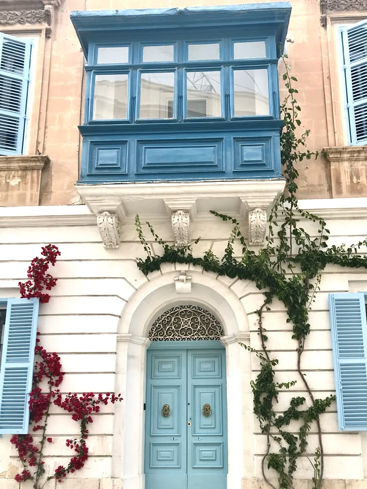 an old building with blue shutters on the front and side doors that have vines growing out of them