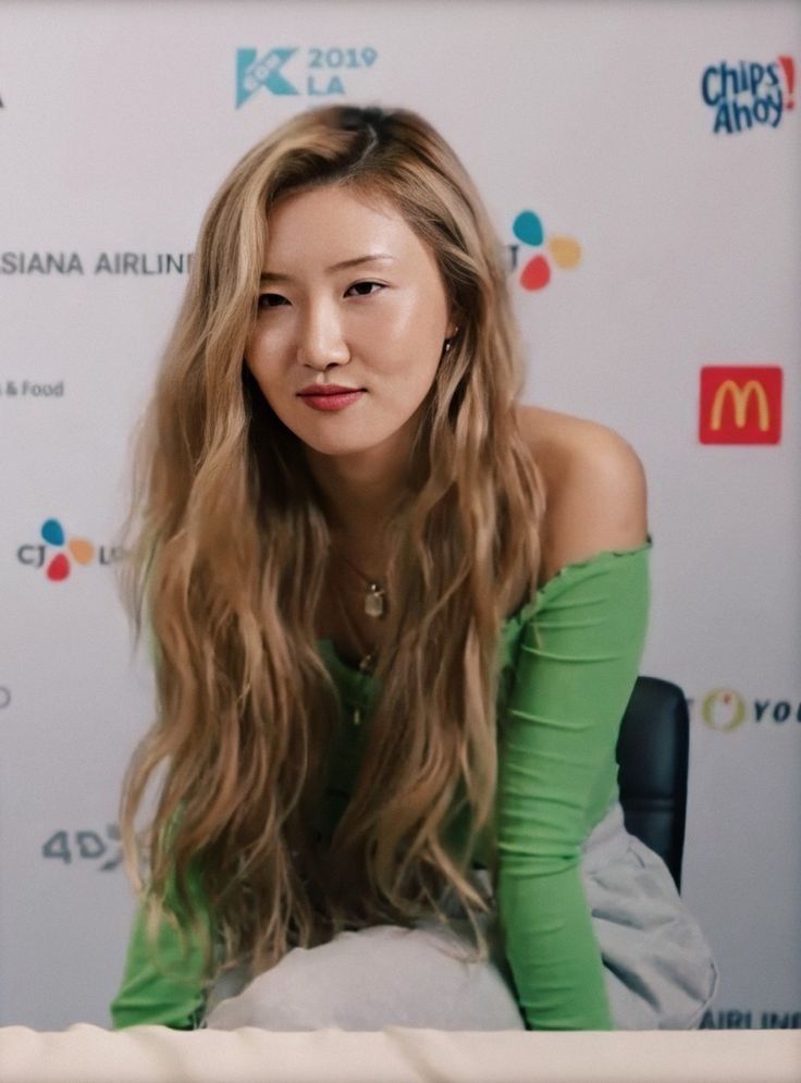 a woman with long hair sitting in front of a white wall and looking at the camera